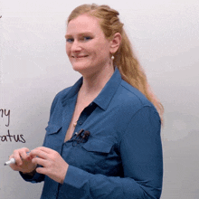 a woman in a blue shirt stands in front of a whiteboard with the word status written in black marker