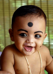 a baby with a black dot on his forehead smiles