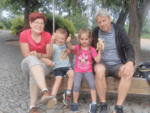 a little girl wearing a minnie mouse shirt is sitting on a bench with her family