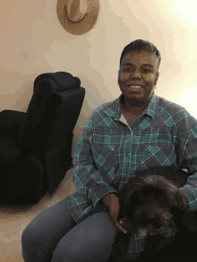 a woman in a plaid shirt sits on a couch holding a small black dog