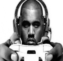 kanye west is wearing headphones and holding a video game controller in his hands .