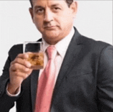 the man is wearing a suit and tie and holding a glass of whiskey .