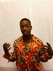 a man wearing glasses and a colorful shirt is standing in front of a white curtain .