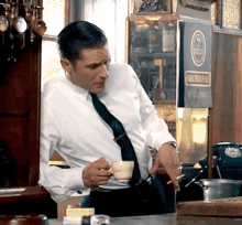 a man in a white shirt and black tie holds a cup of coffee in front of a sign that says dark brown ale