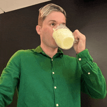 a man wearing a green shirt is drinking from a glass