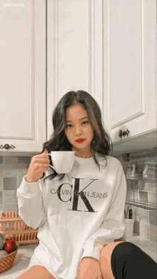 a woman wearing a white calvin klein jeans sweatshirt is holding a cup of coffee