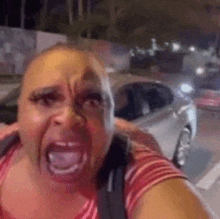 a woman is making a funny face while taking a selfie with a car in the background .