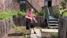 a man in a red shirt and black shorts is standing on a wooden board in front of a brick building .