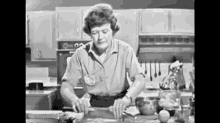 a black and white photo of a woman cutting a piece of meat on a cutting board in a kitchen .