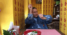 a woman in a denim jacket is sitting at a table with a bowl of food in front of her .