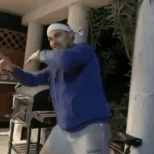 a man wearing a headband and a blue jacket is dancing on a porch .