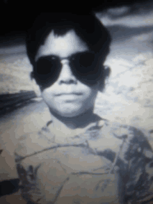 a boy wearing sunglasses looks at the camera in a black and white photo