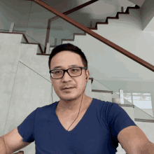 a man wearing glasses and a blue shirt is standing in front of stairs