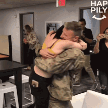 a man in a military uniform is hugging a woman in a room with a sign that says hap pily