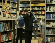 a man in a black suit is talking on a phone in a book store