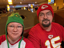 a man and a woman are posing for a picture while wearing a grinch hat and a chiefs jersey