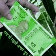 a person is holding a green currency note in their hand with a picture of mahatma gandhi on it .