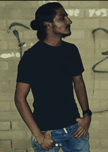 a man wearing a black shirt stands in front of a brick wall with graffiti on it