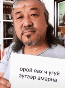 a man with long hair and a beard is holding a piece of paper with a message on it in a foreign language .