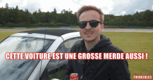 a man holding a can of coca cola in front of a car with the words cette voiture est une grosse merde aussi