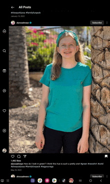 a girl in a teal shirt is standing next to a palm tree