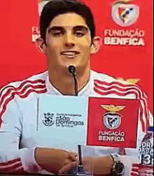 a man speaking into a microphone while holding a sign that says fundacao benfica