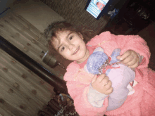 a little girl in a pink coat holds a stuffed animal in her hands