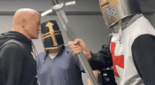 a man in a knight 's helmet is holding a sword in front of a man in a blue shirt .