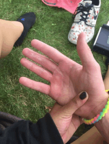 a person with black nail polish is holding another person 's hand in the grass