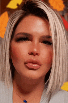 a close up of a woman 's face with blonde hair and a blue necklace