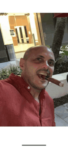 a bald man in a red shirt smoking a cigar