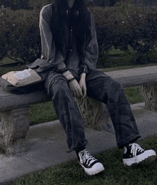 a woman is sitting on a bench in a park wearing black pants and black sneakers .