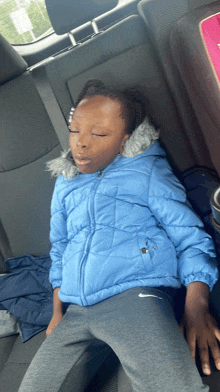 a little girl in a blue jacket is sleeping in a car