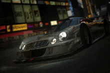 a silver sports car is driving down a city street at night