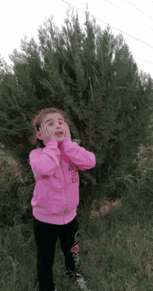 a little girl wearing a pink jacket that says i love you stands in front of a tree