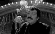 a man is singing into a microphone while smoking a cigarette .