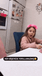 a little girl wearing a pink headband sits at a table in front of a refrigerator with the word her on it