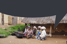 a group of women sit under a thatched roof with alamy written on the bottom left