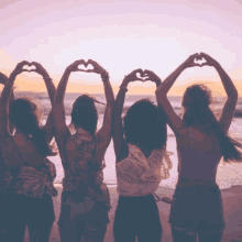 a group of women are making a heart shape with their hands on a beach .