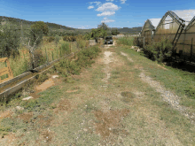 a car is parked on the side of a dirt road next to greenhouses