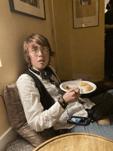 a young boy sits on a couch with a plate of food in front of him