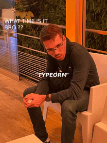 a man wearing glasses sits on a white chair with the words " what time is it bro " written on the bottom