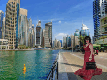 a woman in a red dress is walking by a body of water with a city in the background