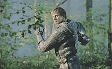 a man in a chain mail armor is walking through a forest .