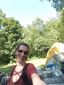 a woman taking a selfie at a picnic table with a tent in the background