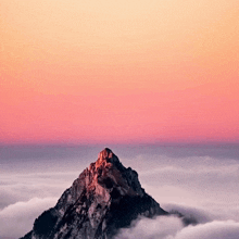 a mountain covered in clouds with a sunset in the background