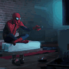 a man in a spiderman costume is sitting on a couch holding a remote control