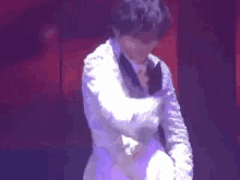 a man in a white suit is dancing on a stage in front of a purple light .