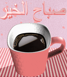 a cup of coffee sits on a checkered table cloth with the words " صباح الخير " written above it