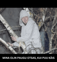 a man in a hoodie is standing in a tree with the words mina olin paugu otsas kui puu kais below him